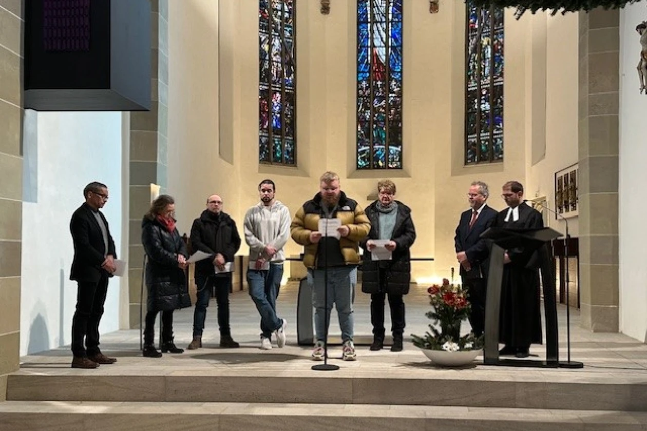 Mehrere Personen stehen im Altarraum einer Kirche. Ein Mann steht am Mikrofon und liest etwas vor.