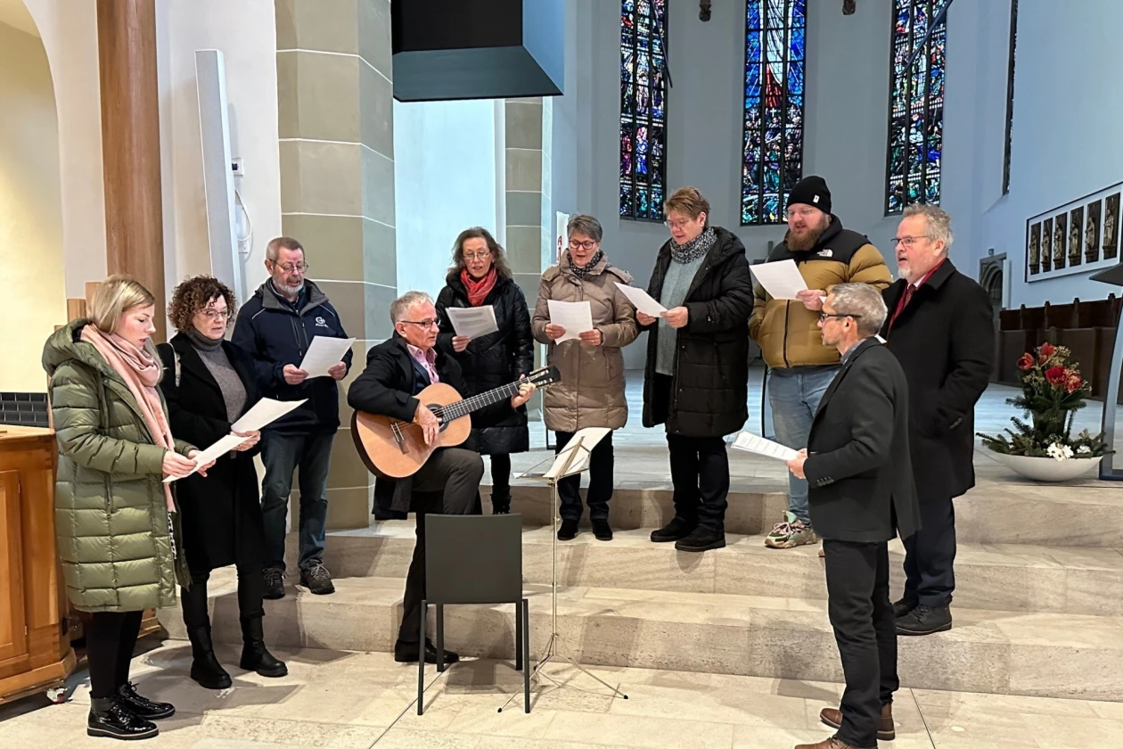 In einer Kirche singt eine Gruppe Menschen, die von einem Mann mit Gitarre begleitet werden.