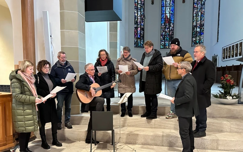 In einer Kirche singt eine Gruppe Menschen, die von einem Mann mit Gitarre begleitet werden.