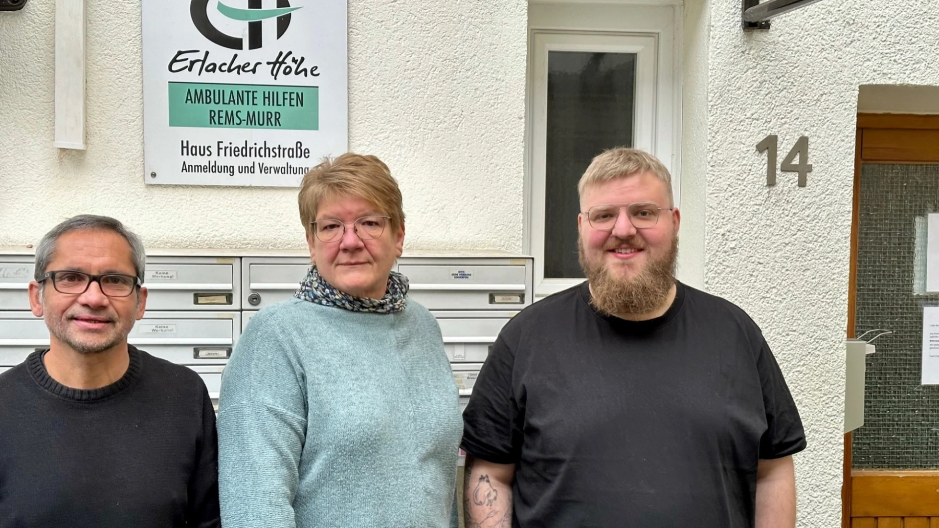 Drei Personen stehen vor einem Geb&auml;ude vor der Briefkastenanlage. An der Wand ist die Nummer 14 sowie ein Schild der Erlacher H&ouml;he mit der Aufschrift "Ambulante Hilfen Rems-Murr" zu sehen.