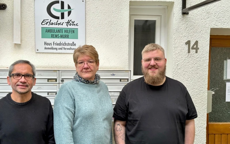 Drei Personen stehen vor einem Geb&auml;ude vor der Briefkastenanlage. An der Wand ist die Nummer 14 sowie ein Schild der Erlacher H&ouml;he mit der Aufschrift "Ambulante Hilfen Rems-Murr" zu sehen.