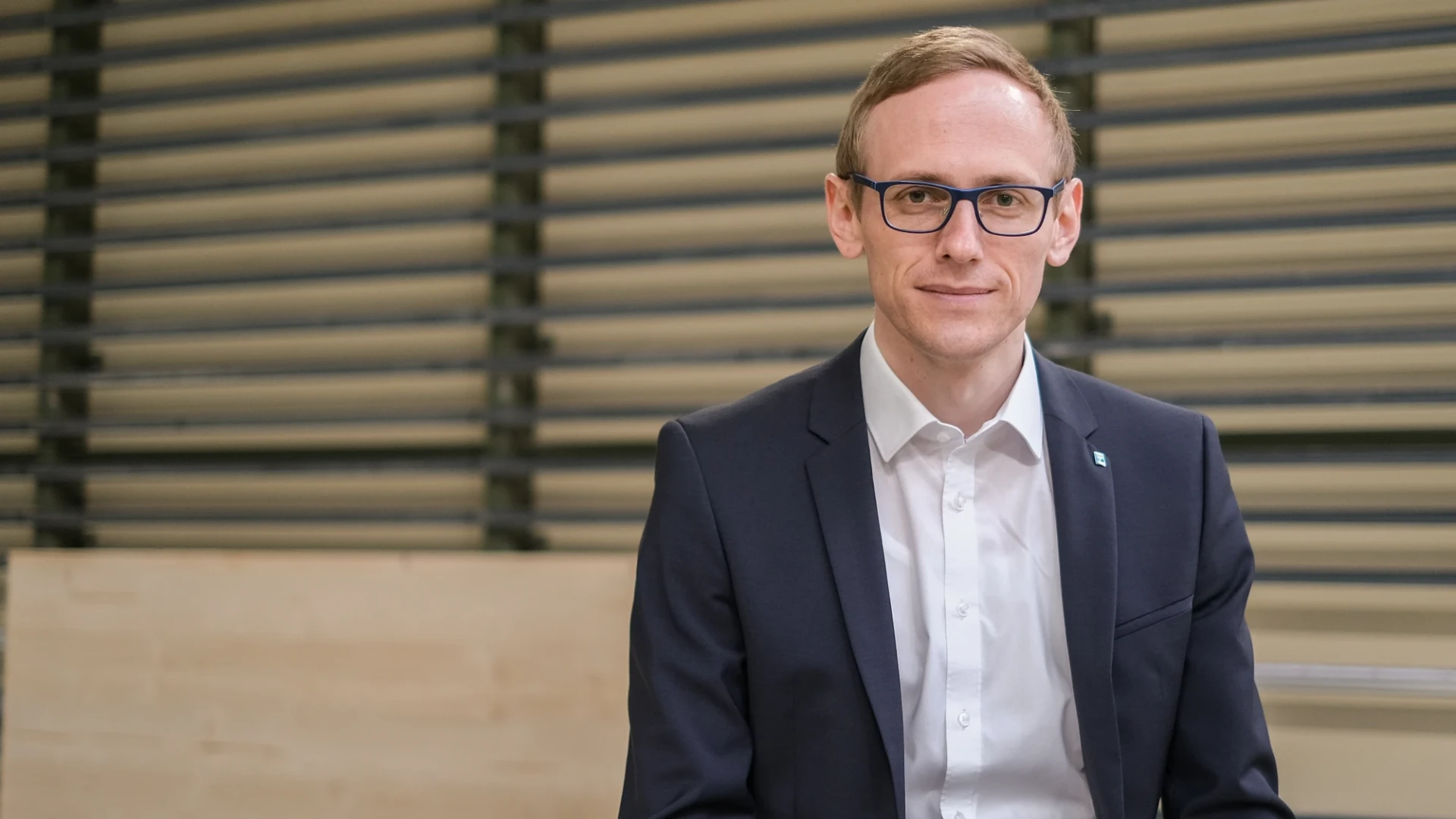 Ein Mann mit Brille, Anzug und wei&szlig;em Hemd blickt l&auml;chelnd in die Kamera.