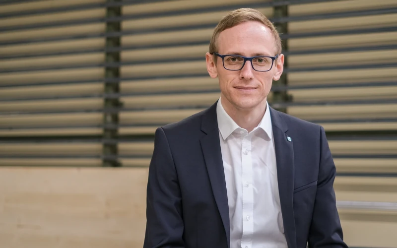 Ein Mann mit Brille, Anzug und wei&szlig;em Hemd blickt l&auml;chelnd in die Kamera.