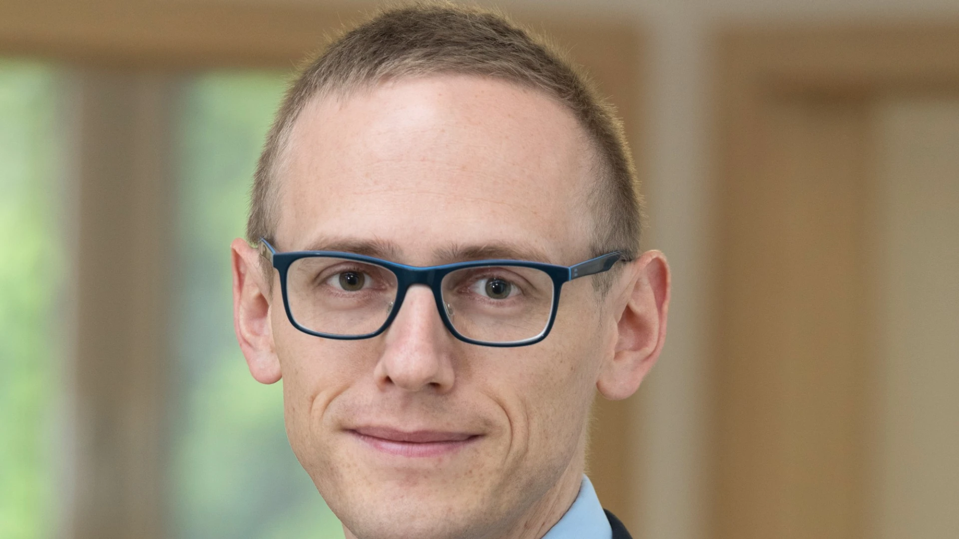 Ein junger Mann mit Brille im dunklen Anzug und hellblauem Hemd. Er tr&auml;gt kurze Haare und schaut direkt in die Kamera.