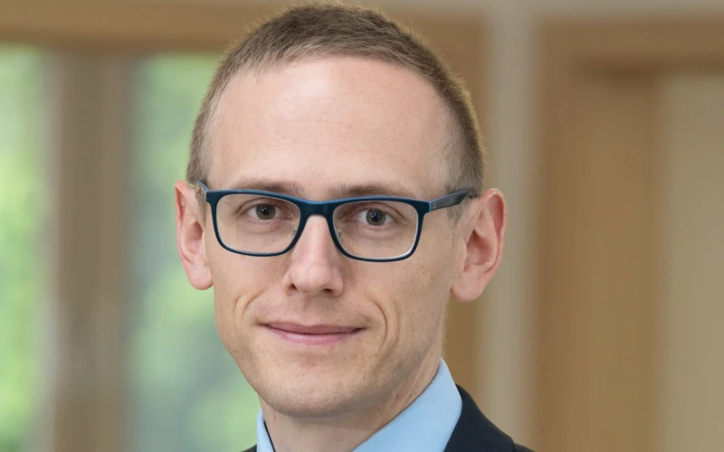 Ein junger Mann mit Brille im dunklen Anzug und hellblauem Hemd. Er tr&auml;gt kurze Haare und schaut direkt in die Kamera.