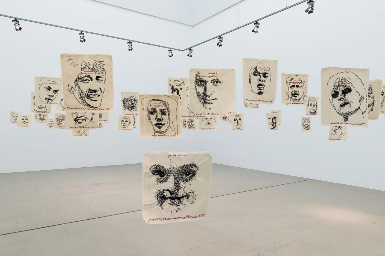 Eine Kunstinstallation mit verschiedenen handgezeichneten Portr&auml;ts in Schwarz-Wei&szlig;. Die Skizzen zeigen verschiedene Gesichtsausdr&uuml;cke und -formen, aufgeh&auml;ngt mit Klammern an Stahlseilen unter Spotlights.