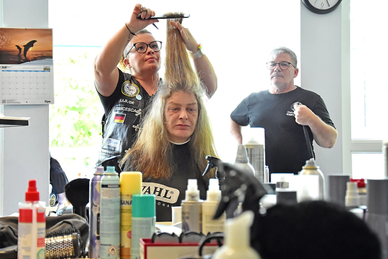 Eine Friseurin schneidet einer Frau mit langen blonden Haaren die Haare