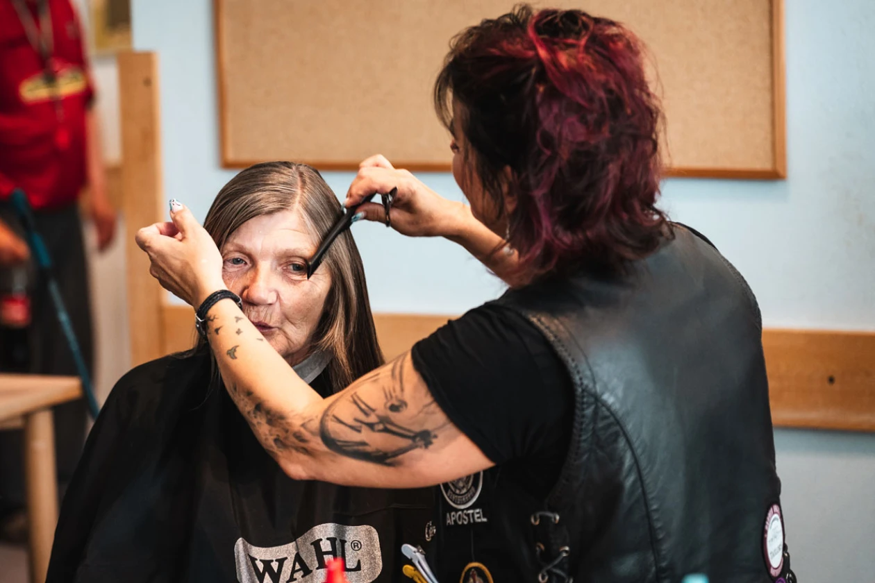 Ein Friseur mit t&auml;towiertem Arm schneidet einer Frau mit dunklem Haar die Haare
