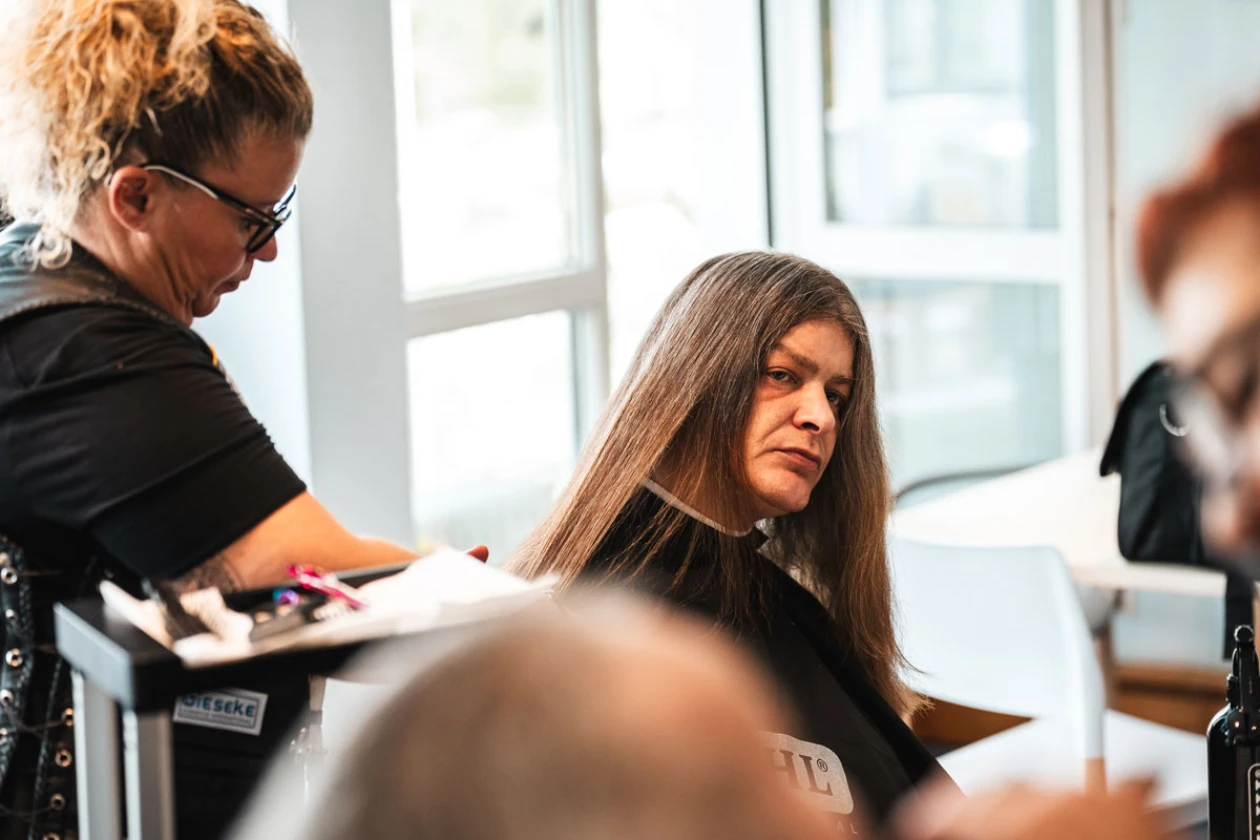 Eine Friseurin schneidet einer Frau mit langen braunen Haaren die Haare in einem hellen Raum