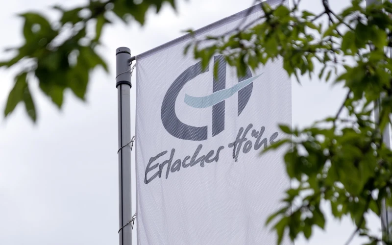 Wei&szlig;e Fahne mit dem Logo und Schriftzug der Erlacher H&ouml;he, vor gr&uuml;nen Bl&auml;ttern und einem bew&ouml;lkten Himmel. Die Flagge zeigt die Webadresse www.erlacher-hoehe.de und einen Kreis mit dem Slogan "Menschen. Leben. W&uuml;rde".