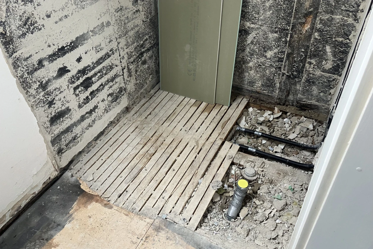 Baustelle in einem Duschbad umgeben von schimmeligen W&auml;nden. Ein Abflussrohr ragt teilweise aus dem Boden.