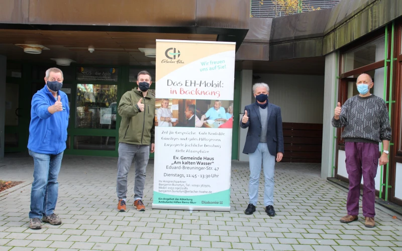 Vier Personen mit Mund-Nasenschutz stehen vor einem Geb&auml;ude auf einem Pflasterboden. Alle zeigen mit den Daumen nach oben. Zwischen ihnen befindet sich ein aufgestellter Banner mit der Aufschrift: "Das EH-Mobil in Backnang".