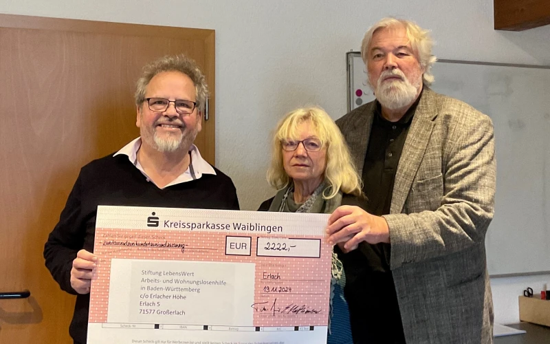 Ein Ehepaar &uuml;bergibt einem Mann mit grauen Haaren und Bart einen Spendenscheck.