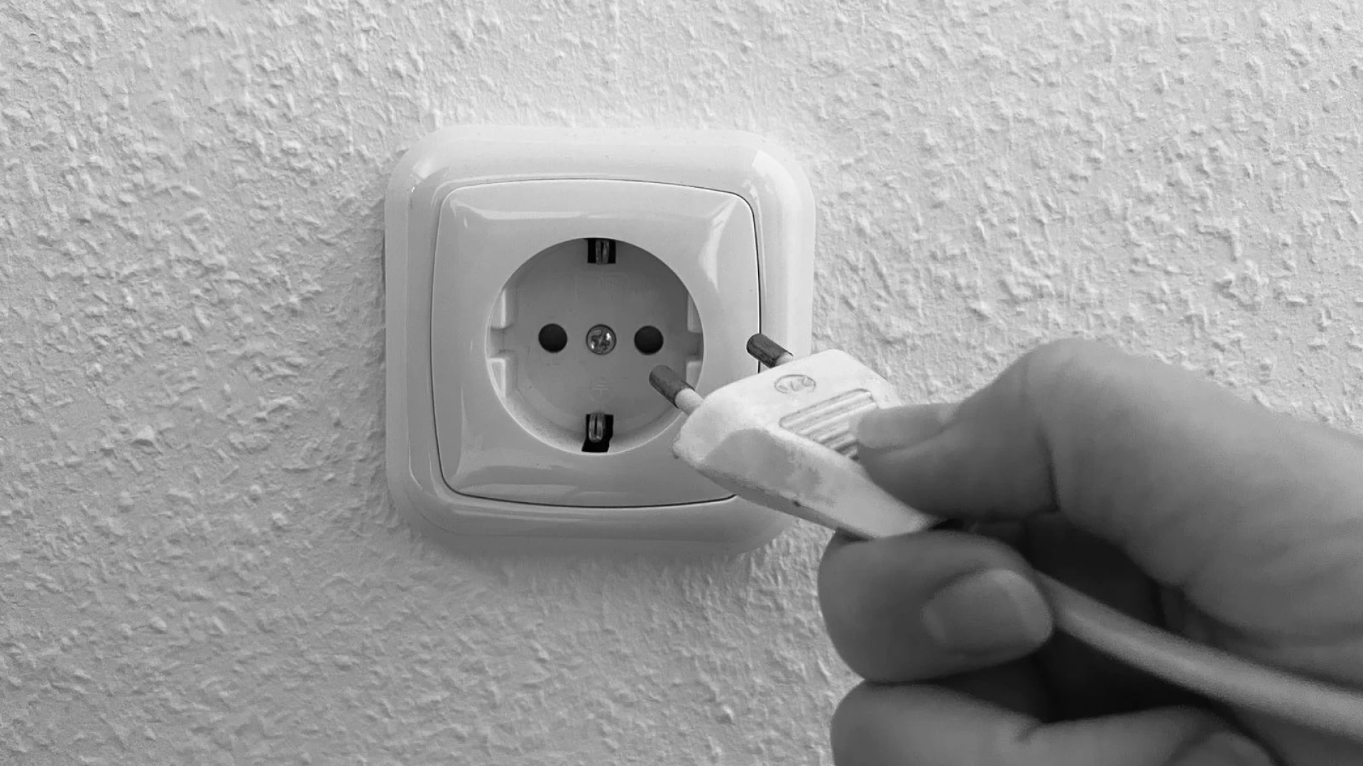 Gro&szlig;aufnahme einer Hand, die einen Stecker eines Ger&auml;tes in eine Steckdose stecken will.