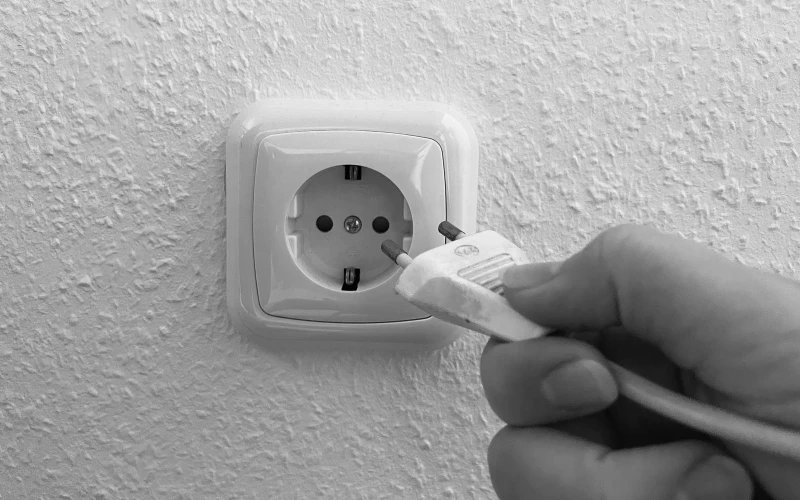 Gro&szlig;aufnahme einer Hand, die einen Stecker eines Ger&auml;tes in eine Steckdose stecken will.