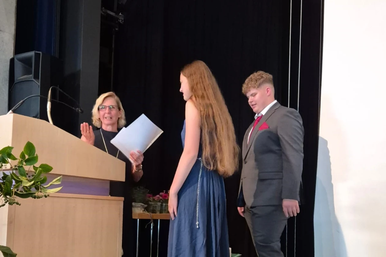 Drei Personen stehen auf einer B&uuml;hne vor einem dunklen Hintergrund