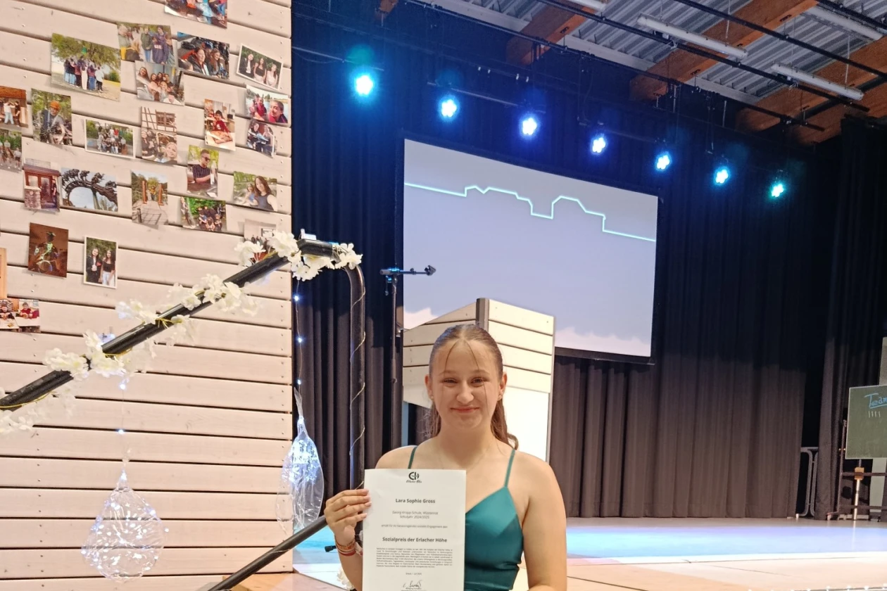 Eine junge Frau in einem gr&uuml;nen Kleid h&auml;lt eine Urkunde auf einer B&uuml;hne und wird f&uuml;r einen Sozialpreis ausgezeichnet