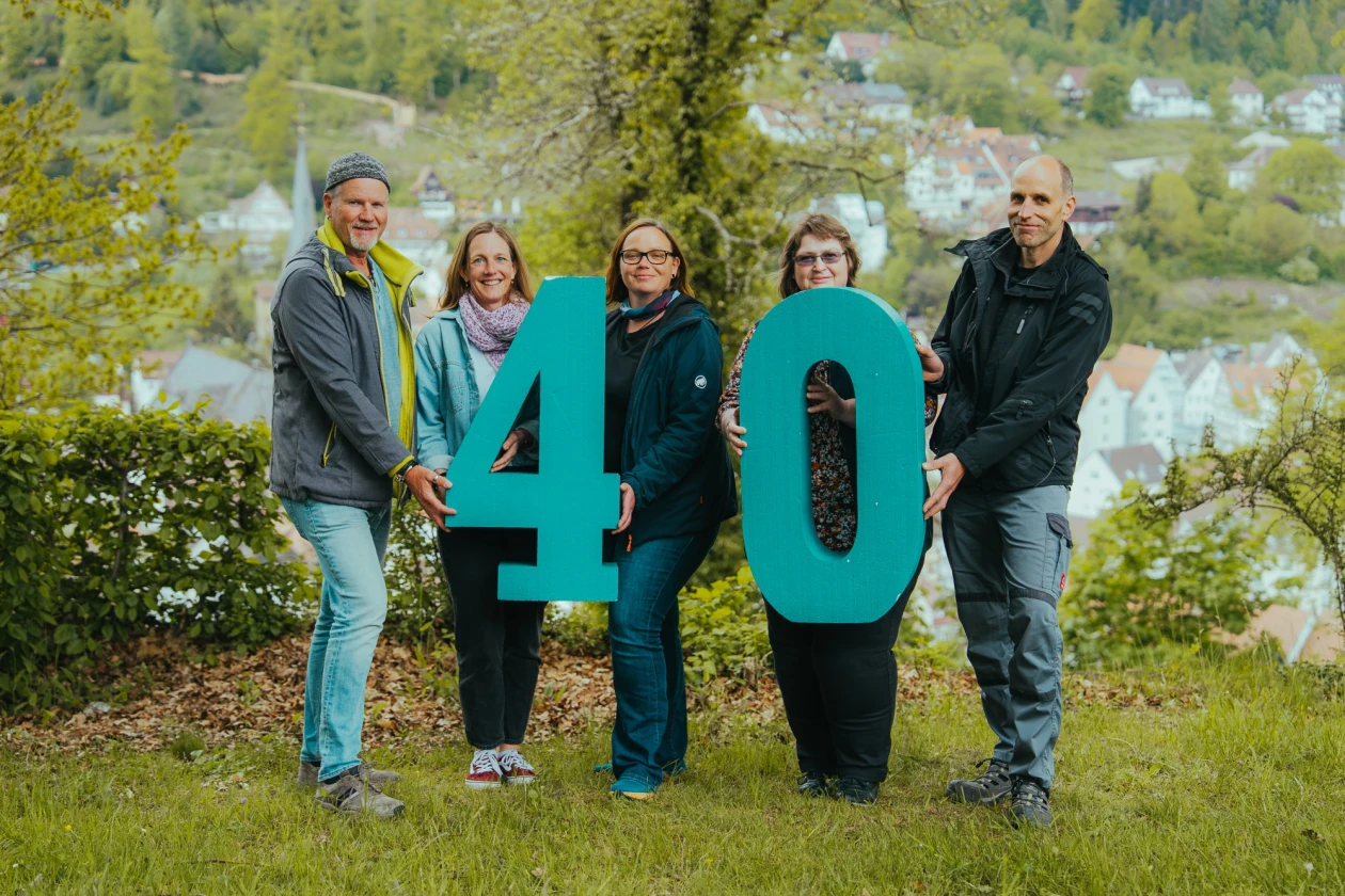 F&uuml;nf Personen stehen nebeneinander auf einer Wiese und halten gro&szlig;e t&uuml;rkisfarbene Zahlen "40" in den H&auml;nden