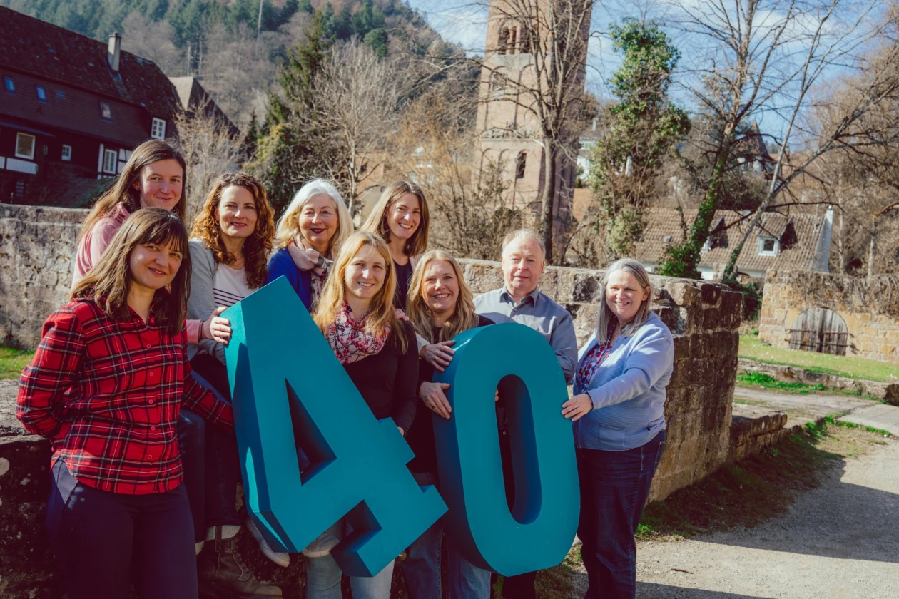 Gruppe von Personen posiert vor einer Kirche mit gro&szlig;en t&uuml;rkisen Zahlen "40" zum Feiern eines Jubil&auml;ums