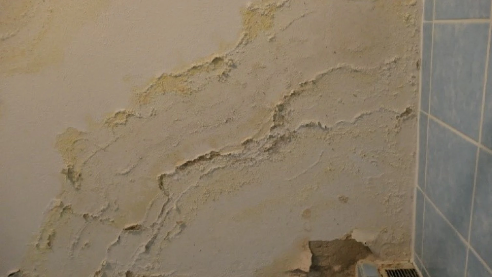 Zu sehen ist eine Badezimmerwand mit abgeplatztem Putz, Verf&auml;rbungen vermutlich durch einen Wasserschaden.