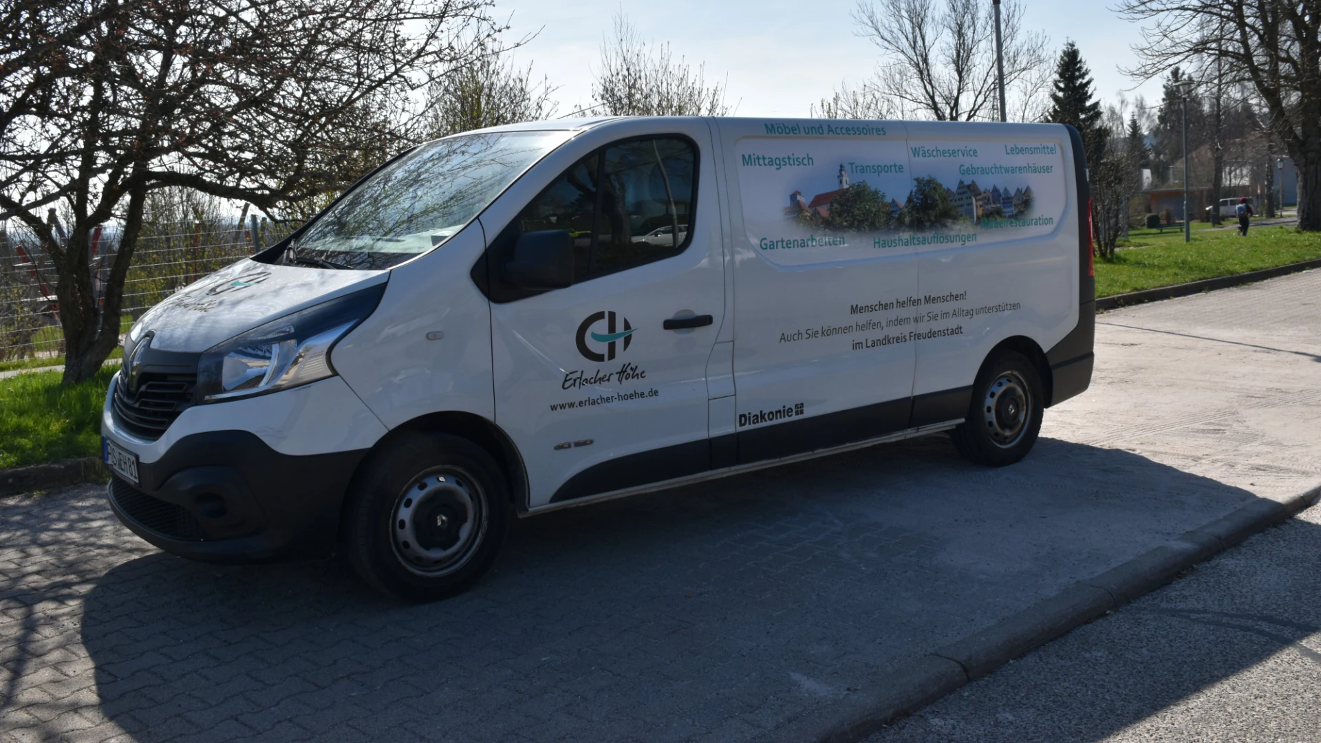 Ein wei&szlig;er Lieferwagen mit dem Logo der ErlacherH&ouml;he" steht auf einem Parkplatz neben kahlen B&auml;umen und gr&uuml;nen Wiesen.