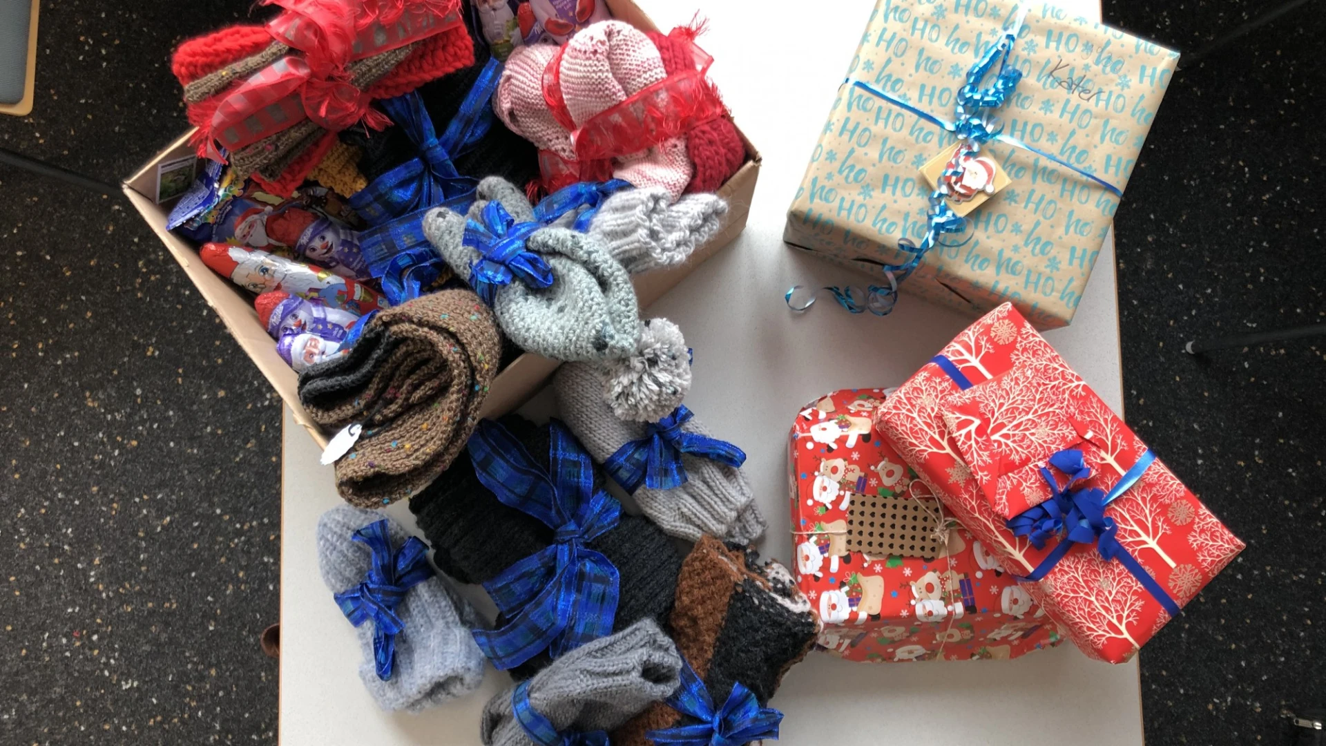 Mehrere Geschenkpakete in verschiedenen Farben und Mustern - rot, blau und gemustert - liegen auf einem wei&szlig;en Untergrund Es sind Strickwaren, die mit blauem Geschenkband versehen sind.