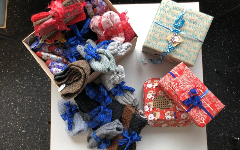 Mehrere Geschenkpakete in verschiedenen Farben und Mustern - rot, blau und gemustert - liegen auf einem wei&szlig;en Untergrund Es sind Strickwaren, die mit blauem Geschenkband versehen sind.