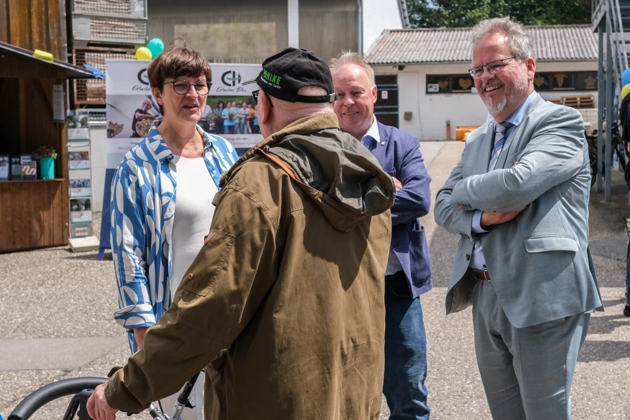 Eine Frau unterh&auml;lt sich mit drei M&auml;nnern auf einer Hoffl&auml;che. Im Hintergrund ist ein geschm&uuml;ckter Infostand zu sehen.