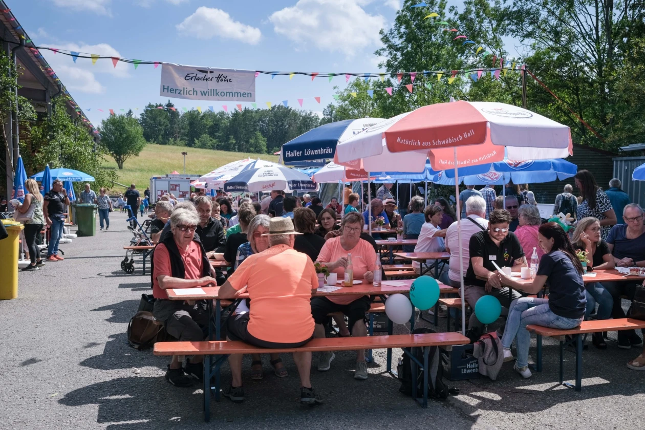 Menschen sitzen auf Bierb&auml;nken unter Sonnenschirmen in gem&uuml;tlicher Festatmosph&auml;re.