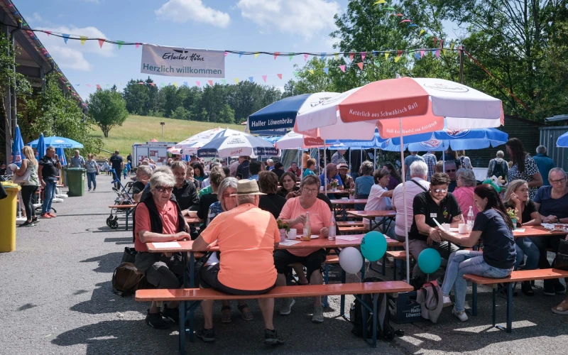 Menschen sitzen auf Bierb&auml;nken unter Sonnenschirmen in gem&uuml;tlicher Festatmosph&auml;re.