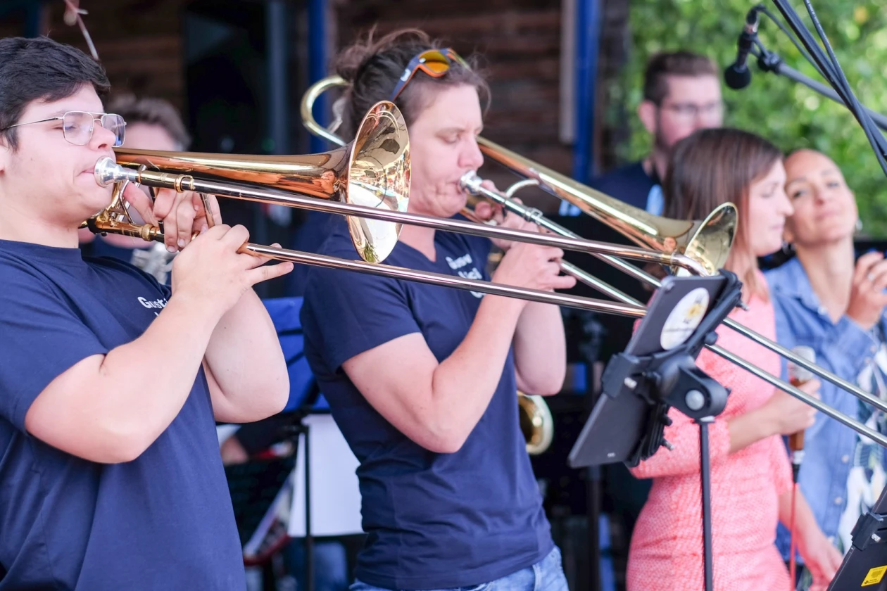 Auf einer B&uuml;hne sind zwei M&auml;nner Posaune spielend zu sehen. Im Hintergrund zwei Frauen, die dazu singen.