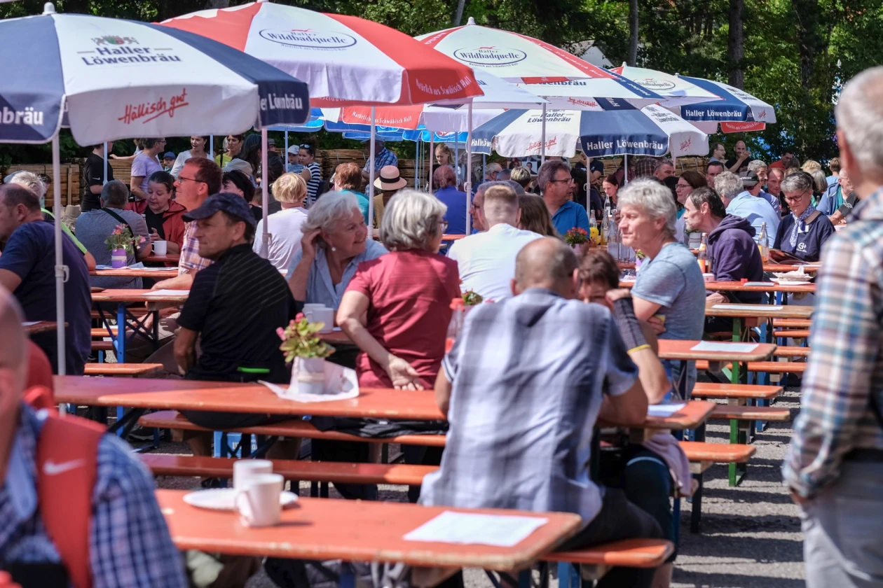 Menschen sitzen auf Bierb&auml;nken unter Sonnenschirmen bei Festbetrieb.  Atmosph&auml;re unter freiem Himmel bei einem Sommerfest.