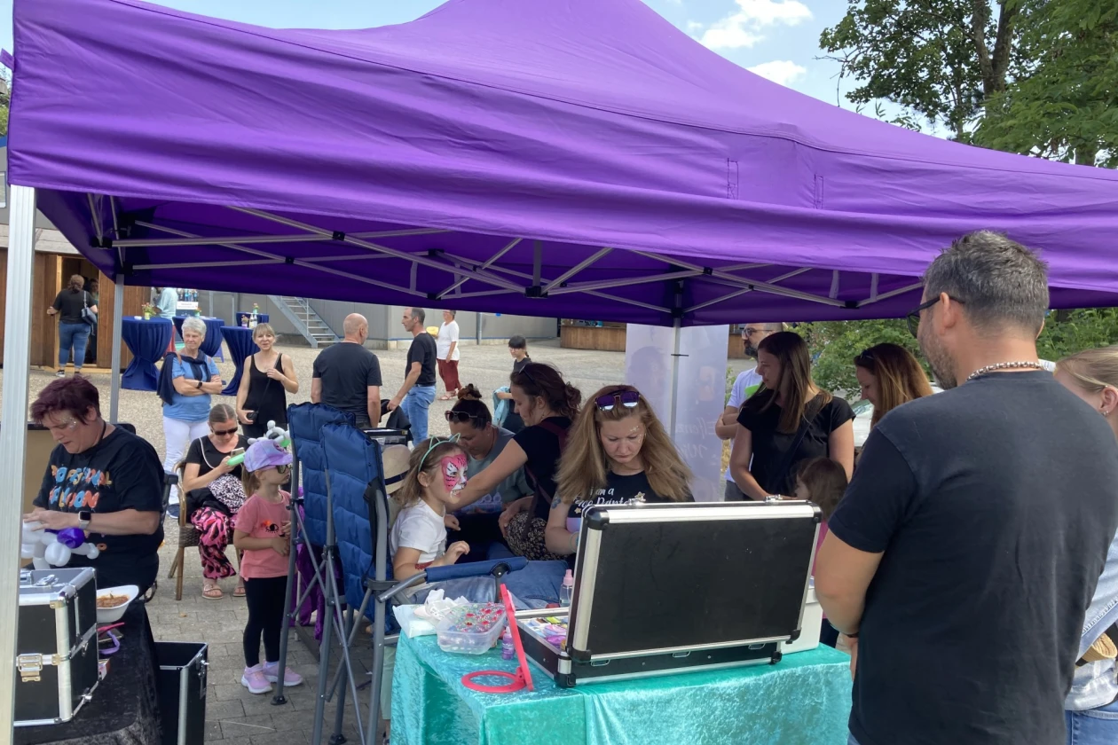 Unter einem Pavillion sitzen Kinder. Diese werden von Frauen im Gesicht geschminkt.