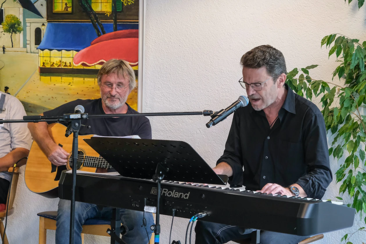 Zwei Musiker sitzen in schwarzer Kleidung auf einer B&uuml;hne. Der Mann am E-Piano singt w&auml;hrend der andere Gitarre spielt.