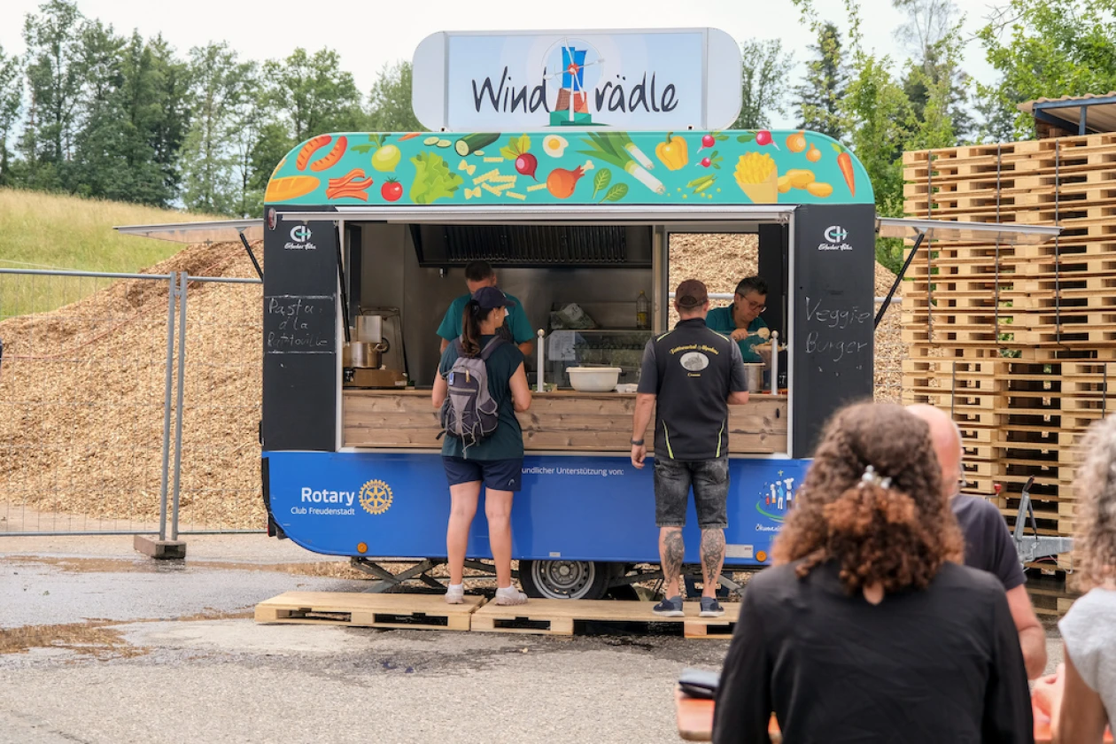 Ein Verkaufsstand "Windr&auml;dle" mit buntem Dach auf einem Fest, an dem mehrere Personen anstehen