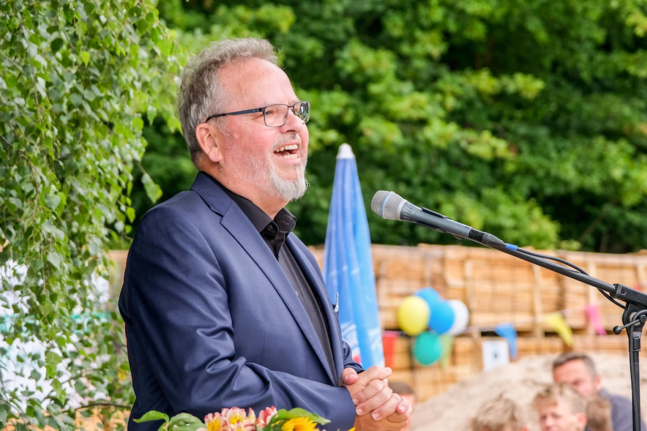Wolfgang Sartorius spricht an einem Mikrofon vor einer gr&uuml;nen Hecke. Im Hintergrund sind bunte Ballons und Zuschauer bei einem Fest zu sehen.