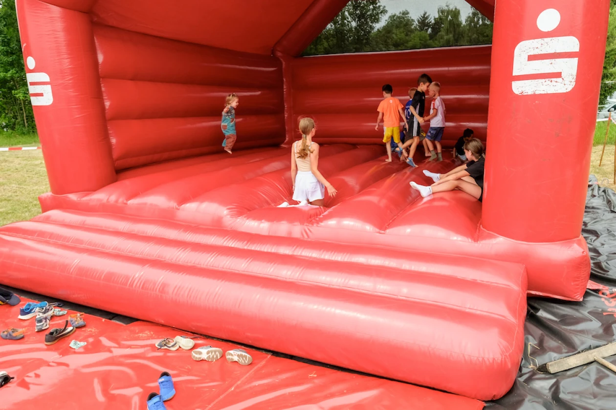Kinder spielen in einer roten aufblasbaren H&uuml;pfburg auf einem Rasenplatz