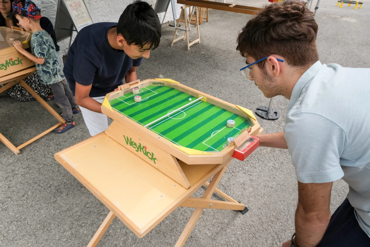 Zwei Jungen spielen an einem Tischkicker auf einer Holzplattform w&auml;hrend eines Festes