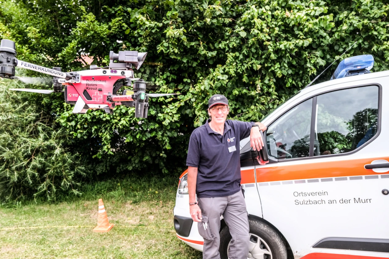 Ein Mitarbeiter der Rettungsdienste steht neben einem orange-wei&szlig;en Einsatzfahrzeug des Ortsvereins Sulzbach an der Murr