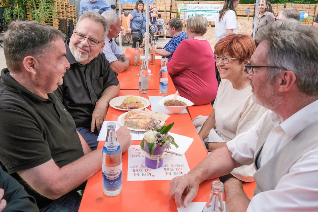 Eine Gruppe von Menschen sitzt an einem Tisch bei einem Fest und unterh&auml;lt sich bei Mahlzeiten und Getr&auml;nken