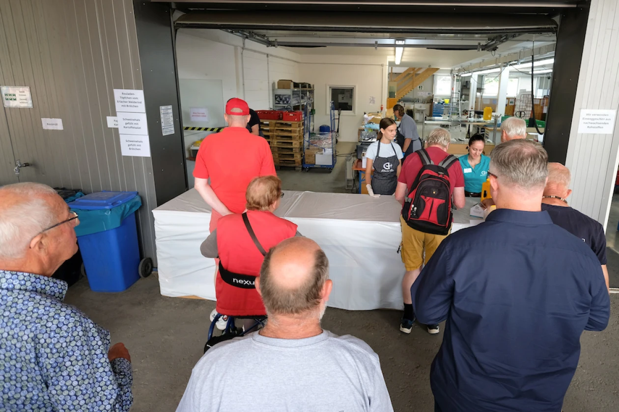 Eine Gruppe von Besuchern steht vor einem Ausgabestand mit der Aufschrift "Essensausgabe" bei einem Fest