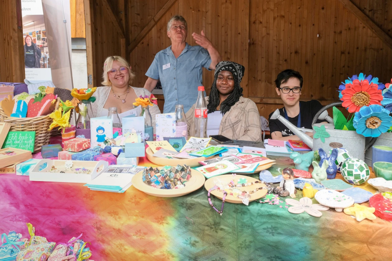Vier Personen sitzen und stehen an einem Tisch mit bunten Bastelarbeiten