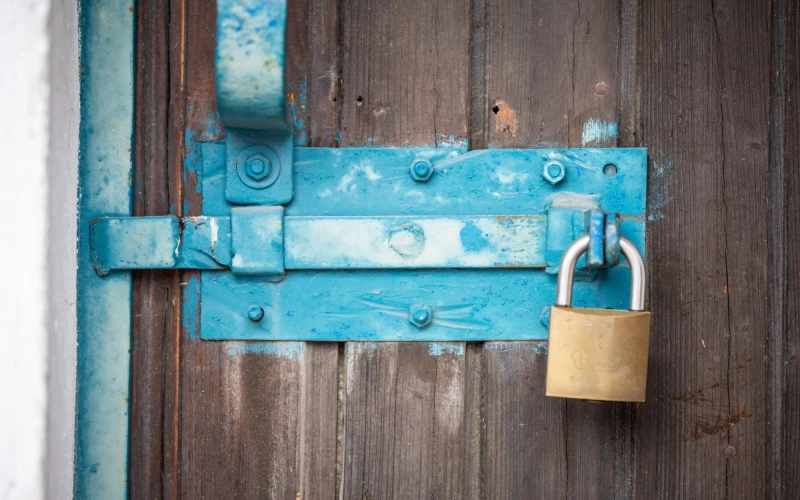 Zu sehen ist eine geschlossene Holzt&uuml;r mit t&uuml;rkisfarbenem Beschlag und Riegel und mit einem Vorh&auml;ngeschloss.