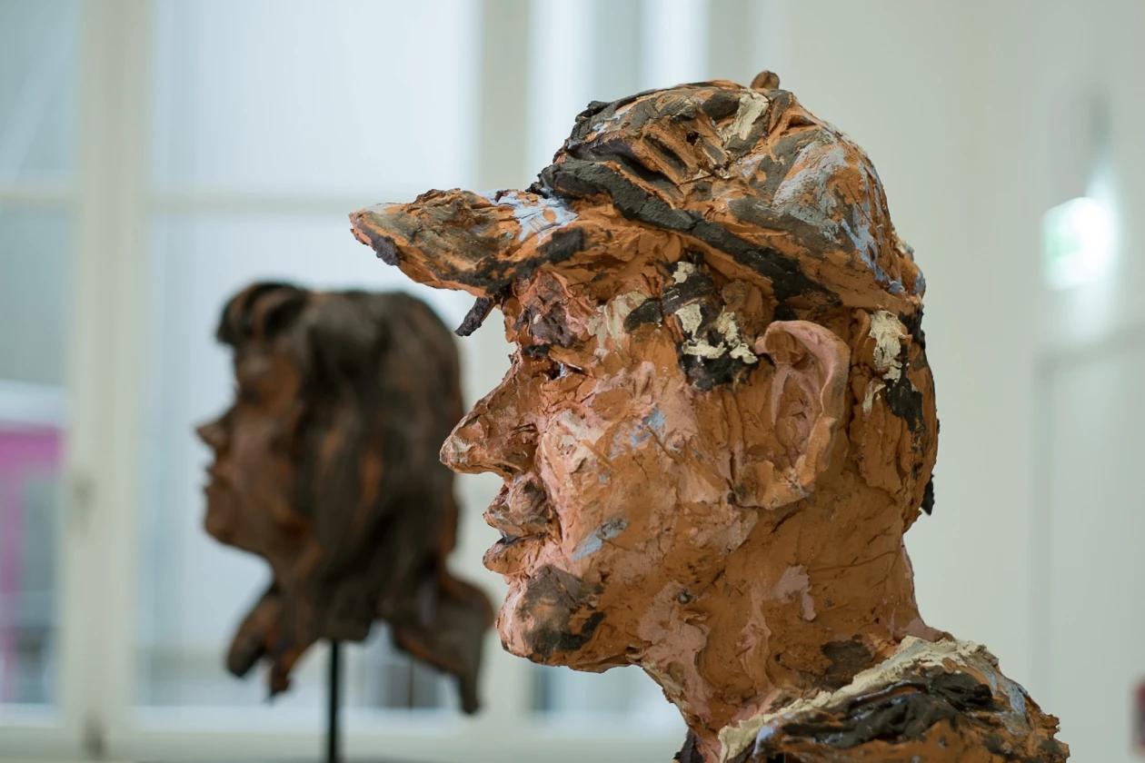 Zwei Kopfskulpturen aus Ton, die ein menschliches Gesicht darstellt. Die Skulptur steht vor einem unscharfen Hintergrund mit einem Fenster.