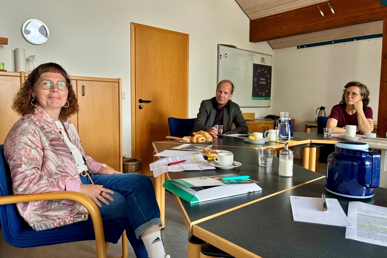 Drei Personen sitzen an einem Konferenztisch in einem Besprechungsraum