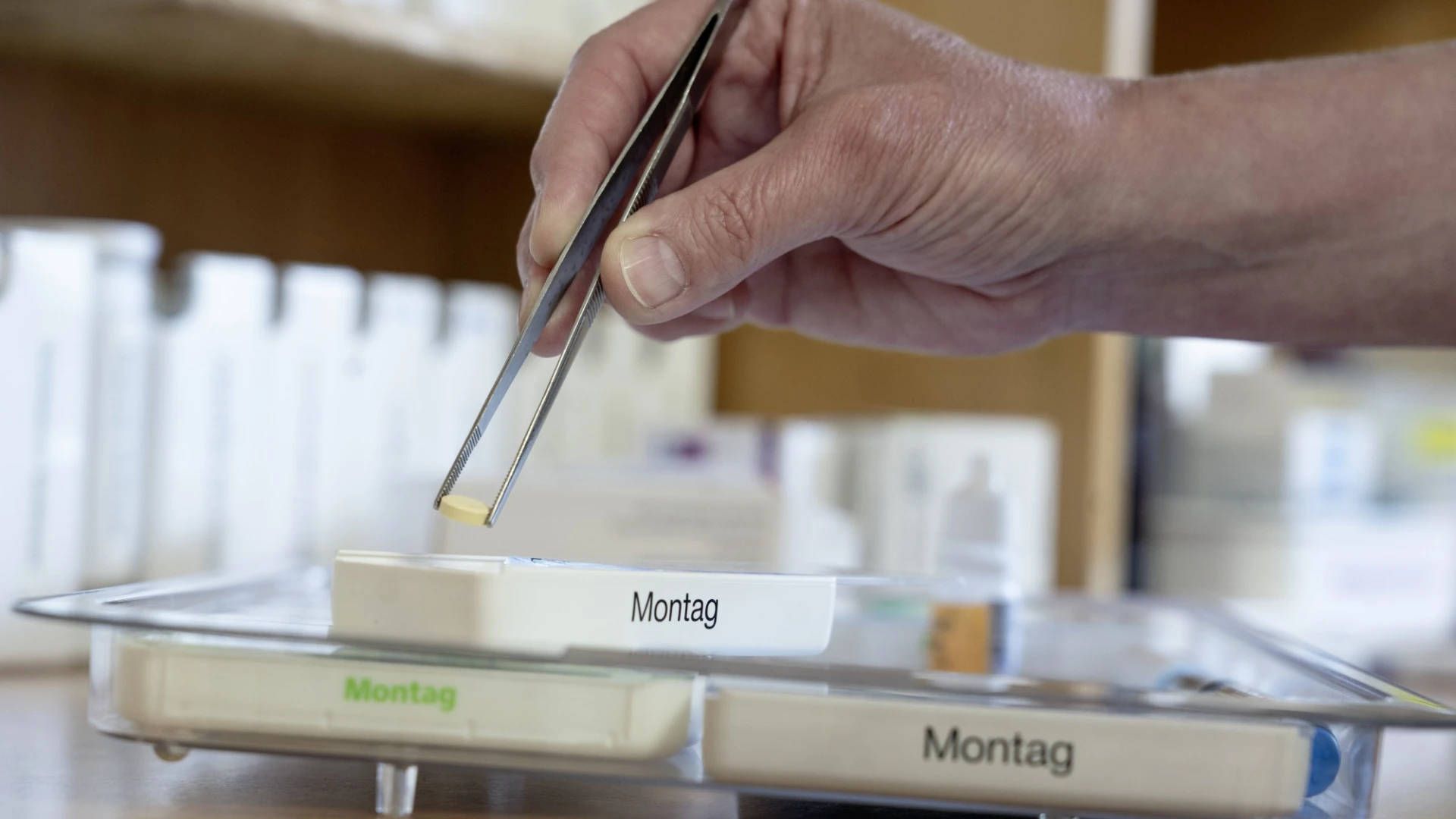 Eine Person verteilt Tabletten mit einer Pinzette in einen Tablettendispenser.