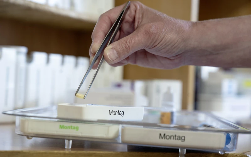 Eine Person verteilt Tabletten mit einer Pinzette in einen Tablettendispenser.