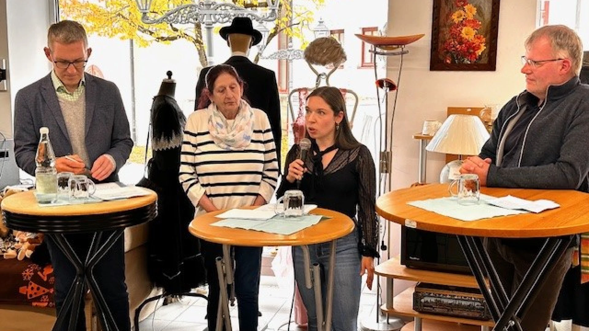 F&uuml;nf Personen stehen in einem hellen Raum an hohen Stehtischen und sprechen miteinander