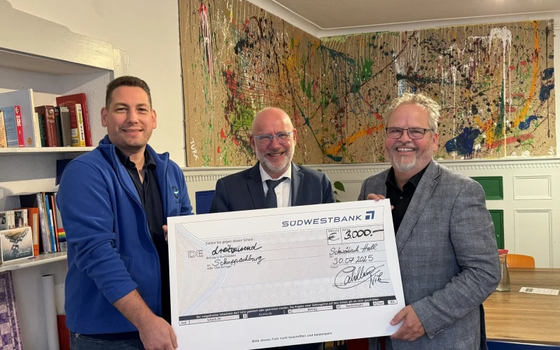 Drei M&auml;nner halten gemeinsam einen gro&szlig;en Scheck mit der Aufschrift "S&uuml;dwestbank" in einem B&uuml;ro