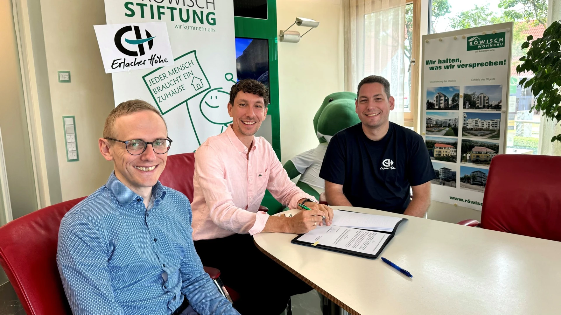 Drei M&auml;nner sitzen an einem Tisch mit Dokumenten. Es scheint sich um die Unterzeichnung eines Vertrages zu handeln. Alle drei M&auml;nner blicken freudig l&auml;chelnd in die Kamera.